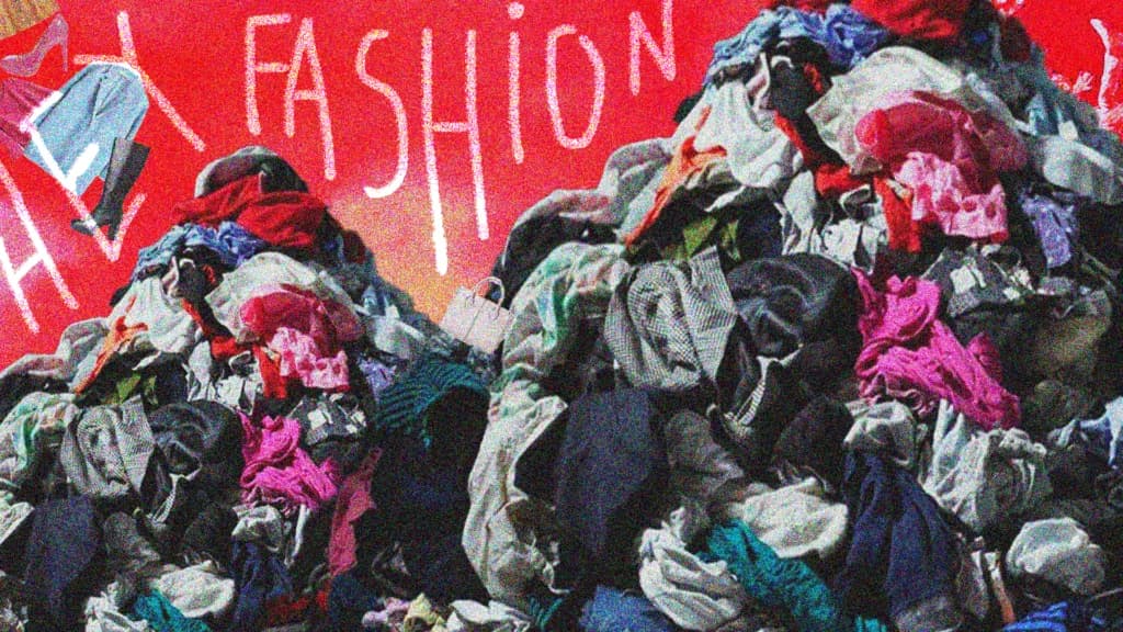 A heap of discarded clothing against a red wall painted with the word fashion
